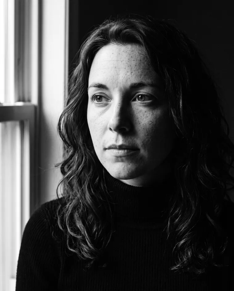 Portrait noir et blanc en gros plan d’une femme en col roulé, avec une lumière latérale dure depuis une fenêtre
